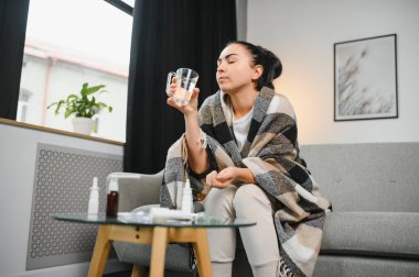 Hasta bir kadın evde kanepede oturan bir baş ağrısı ile gri battaniyeye sarılmış.