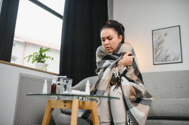 Hasta bir kadın evde kanepede oturan bir baş ağrısı ile gri battaniyeye sarılmış.