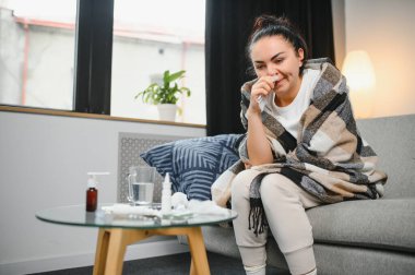 Genç bir kadın kanepeye oturur, battaniyeyle kaplanır, donar, burnunu siler, mendile hapşırır. Kadın ateşlendi, grip oldu ve grip belirtileri evde öksürüyor. Solunum hastalığına alerjim var..