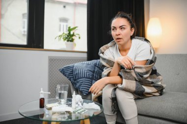 Genç bir kadın kanepeye oturur, battaniyeyle kaplanır, donar, burnunu siler, mendile hapşırır. Kadın ateşlendi, grip oldu ve grip belirtileri evde öksürüyor. Solunum hastalığına alerjim var..