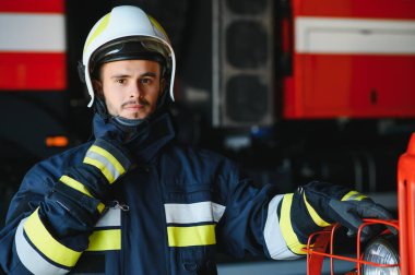 Görevdeyken itfaiyeci portresi. İtfaiye arabasının yanında gaz maskesi ve miğferi olan itfaiyeci.