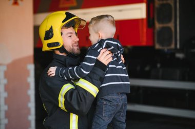 Bir itfaiyeci küçük bir çocuğu kurtarmak için kaçırıyor. Arka planda itfaiye arabası var. Kollarında çocuk olan itfaiyeci. Koruma kavramı