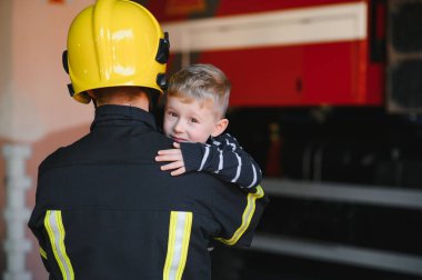 Kirli itfaiyeci siyah arka planda duran kurtarılmış küçük çocuğu tutuyor.