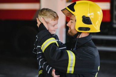 Kirli itfaiyeci siyah arka planda duran kurtarılmış küçük çocuğu tutuyor.
