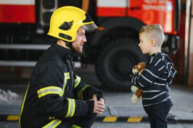 İtfaiyeciyle birlikte kurtarılmış küçük bir çocuğun portresi itfaiye aracının yanında duruyor. İtfaiyeci itfaiye operasyonunda.