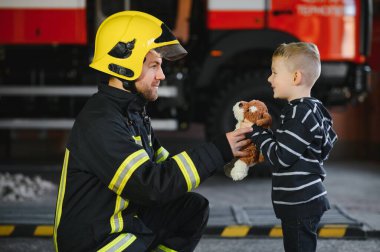 İtfaiyeciyle birlikte kurtarılmış küçük bir çocuğun portresi itfaiye aracının yanında duruyor. İtfaiyeci itfaiye operasyonunda.