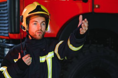 Görevdeyken itfaiyeci portresi. İtfaiye arabasının yanında gaz maskesi ve miğferi olan itfaiyeci.