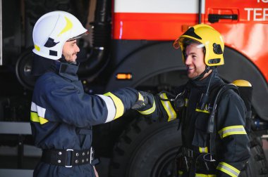 Koruyucu giysili, kasklı, itfaiye arabalı, dost canlısı iki itfaiyeci..