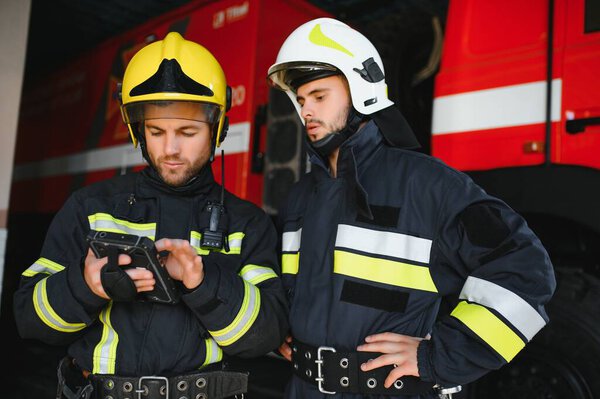 Portrait of two firefighters in fire fighting operation, fireman in protective clothing and helmet using tablet computer in action fighting.