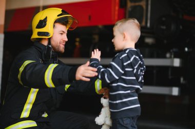 Kirli itfaiyeci siyah arka planda duran kurtarılmış küçük çocuğu tutuyor.