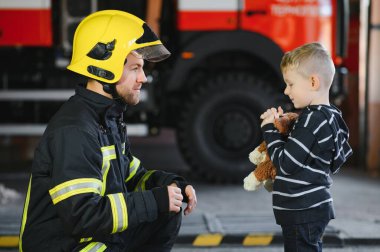 Bir itfaiyeci küçük bir çocuğu kurtarmak için kaçırıyor. Arka planda itfaiye arabası var. Kollarında çocuk olan itfaiyeci. Koruma kavramı