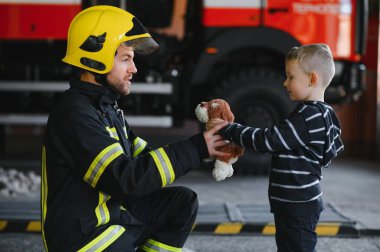 İtfaiyeciyle birlikte kurtarılmış küçük bir çocuğun portresi itfaiye aracının yanında duruyor. İtfaiyeci itfaiye operasyonunda.