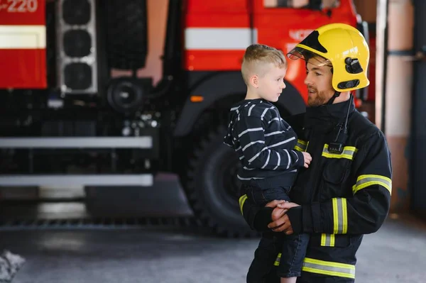 Dirty firefighter in uniform holding little saved boy standing on black background