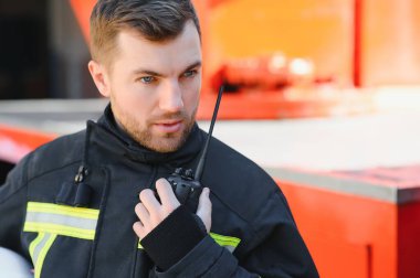 Görevdeyken itfaiyeci portresi. İtfaiye arabasının yanında gaz maskesi ve miğferi olan itfaiyeci.