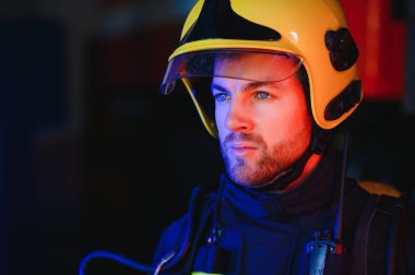 Görevdeyken itfaiyeci portresi. İtfaiye arabasının yanında gaz maskesi ve miğferi olan itfaiyeci.