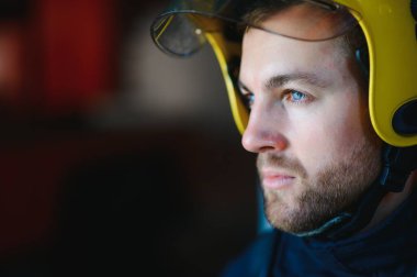 Görevdeyken itfaiyeci portresi. İtfaiye arabasının yanında gaz maskesi ve miğferi olan itfaiyeci.