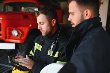 İtfaiye operasyonundaki iki itfaiyecinin portresi. Koruyucu giysili ve kasklı itfaiyeci. Eylem savaşında tablet bilgisayar kullanıyor..