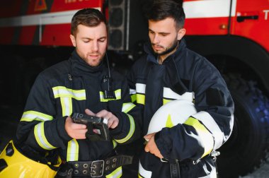 İtfaiye operasyonundaki iki itfaiyecinin portresi. Koruyucu giysili ve kasklı itfaiyeci. Eylem savaşında tablet bilgisayar kullanıyor..