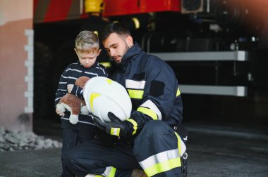 İtfaiyeciyle birlikte kurtarılmış küçük bir çocuğun portresi itfaiye aracının yanında duruyor. İtfaiyeci itfaiye operasyonunda.