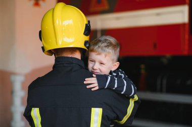 İtfaiyeciyle birlikte kurtarılmış küçük bir çocuğun portresi itfaiye aracının yanında duruyor. İtfaiyeci itfaiye operasyonunda.