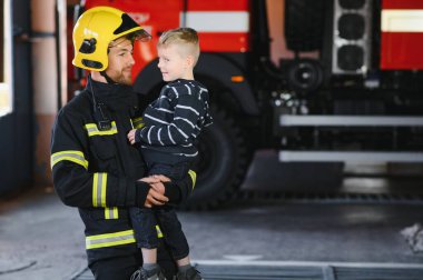 İtfaiyeciyle birlikte kurtarılmış küçük bir çocuğun portresi itfaiye aracının yanında duruyor. İtfaiyeci itfaiye operasyonunda.