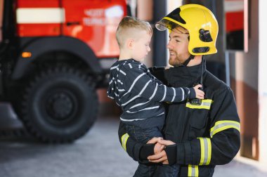 Kirli itfaiyeci siyah arka planda duran kurtarılmış küçük çocuğu tutuyor.