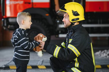 İtfaiyeciyle birlikte kurtarılmış küçük bir çocuğun portresi itfaiye aracının yanında duruyor. İtfaiyeci itfaiye operasyonunda.