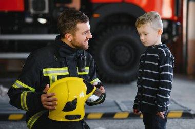 Bir itfaiyeci küçük bir çocuğu kurtarmak için kaçırıyor. Arka planda itfaiye arabası var. Kollarında çocuk olan itfaiyeci. Koruma kavramı