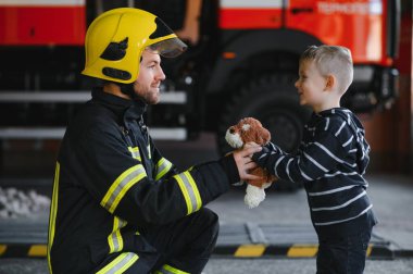 İtfaiyeciyle birlikte kurtarılmış küçük bir çocuğun portresi itfaiye aracının yanında duruyor. İtfaiyeci itfaiye operasyonunda.