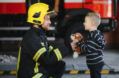 Kirli itfaiyeci siyah arka planda duran kurtarılmış küçük çocuğu tutuyor.