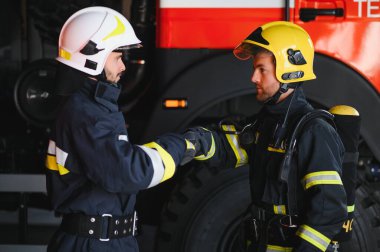 Koruyucu giysili, kasklı, itfaiye arabalı, dost canlısı iki itfaiyeci..