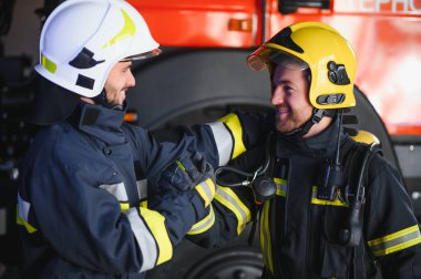 Koruyucu giysili, kasklı, itfaiye arabalı, dost canlısı iki itfaiyeci..