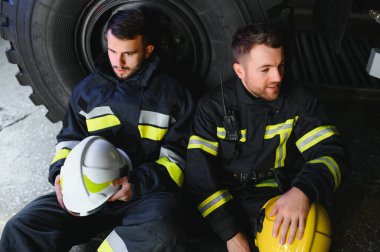 İtfaiye aracının önünde duran üniformalı ve kasklı iki profesyonel itfaiyeci.