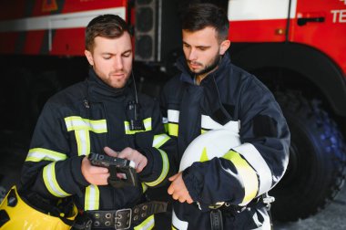 İtfaiye operasyonundaki iki itfaiyecinin portresi. Koruyucu giysili ve kasklı itfaiyeci. Eylem savaşında tablet bilgisayar kullanıyor..