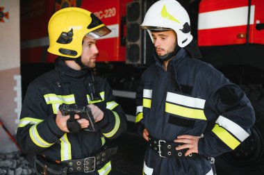 İtfaiye operasyonundaki iki itfaiyecinin portresi. Koruyucu giysili ve kasklı itfaiyeci. Eylem savaşında tablet bilgisayar kullanıyor..