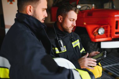 İtfaiye operasyonundaki iki itfaiyecinin portresi. Koruyucu giysili ve kasklı itfaiyeci. Eylem savaşında tablet bilgisayar kullanıyor..