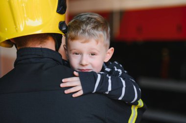 İtfaiyeciyle birlikte kurtarılmış küçük bir çocuğun portresi itfaiye aracının yanında duruyor. İtfaiyeci itfaiye operasyonunda.