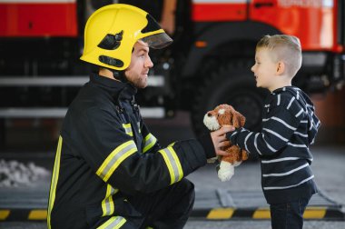 Bir itfaiyeci küçük bir çocuğu kurtarmak için kaçırıyor. Arka planda itfaiye arabası var. Kollarında çocuk olan itfaiyeci. Koruma kavramı