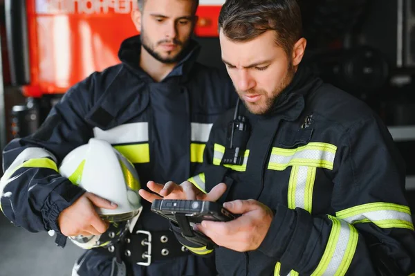 İtfaiye operasyonundaki iki itfaiyecinin portresi. Koruyucu giysili ve kasklı itfaiyeci. Eylem savaşında tablet bilgisayar kullanıyor..