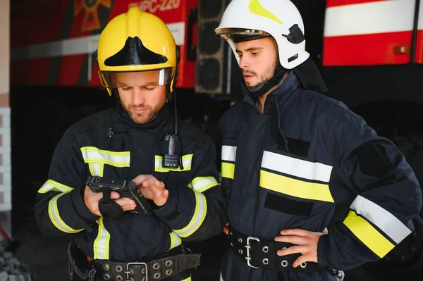 İtfaiye operasyonundaki iki itfaiyecinin portresi. Koruyucu giysili ve kasklı itfaiyeci. Eylem savaşında tablet bilgisayar kullanıyor..
