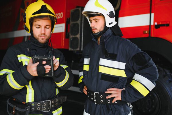 Portrait of two firefighters in fire fighting operation, fireman in protective clothing and helmet using tablet computer in action fighting.