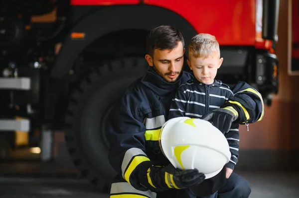 与消防员站在消防车旁边的被救小男孩的画像 消防行动中的消防员 — 图库照片