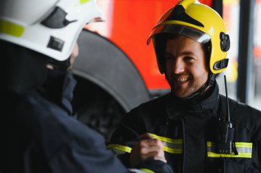 İtfaiye aracının önünde duran üniformalı ve kasklı iki profesyonel itfaiyeci.