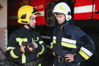 İtfaiye operasyonundaki iki itfaiyecinin portresi. Koruyucu giysili ve kasklı itfaiyeci. Eylem savaşında tablet bilgisayar kullanıyor..