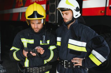 İtfaiye operasyonundaki iki itfaiyecinin portresi. Koruyucu giysili ve kasklı itfaiyeci. Eylem savaşında tablet bilgisayar kullanıyor..