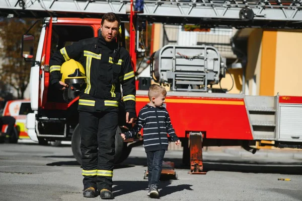 Strażak Zabiera Małego Chłopca Żeby Uratować Samochód Strażacki Tle Strażak — Zdjęcie stockowe
