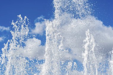 Güçlü jet ve su damlaları fıskiyeden düşer mavi bulutlu yaz gökyüzünün arka planına.