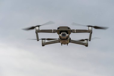 Küçük bir kuadkopter gri gökyüzüne karşı alçak irtifada uçuyor ve kamera fotoğrafçıyı hedef alıyor..