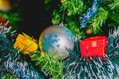 Yeşil bir şenlik ağacındaki parlak Noel süslemeleri: renkli toplar, çelenkler, süsler ve çok renkli hediye kutuları.