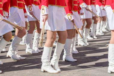 Large group of young girls in red and white ceremonial suits march in formation on city street. Festive procession of drummers. Side view.